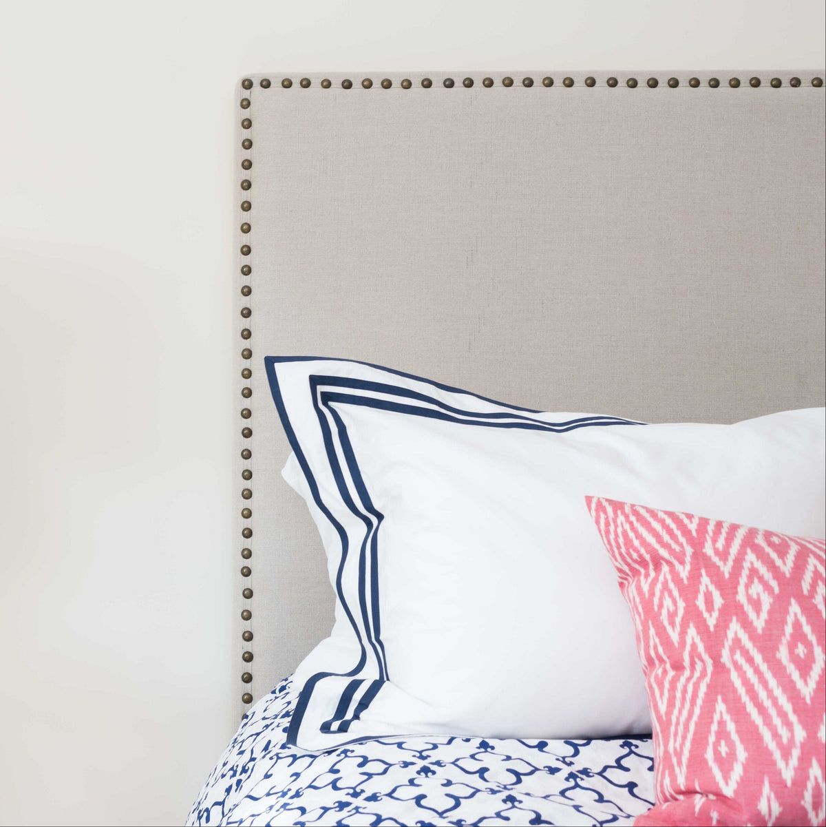 Neatly made bed with decorative pillows against a beige headboard, lamp on nightstand.