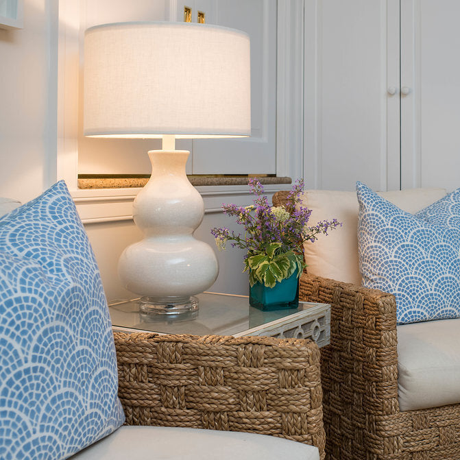 Wicker chairs with patterned cushions and a lamp in a room with white cabinets.