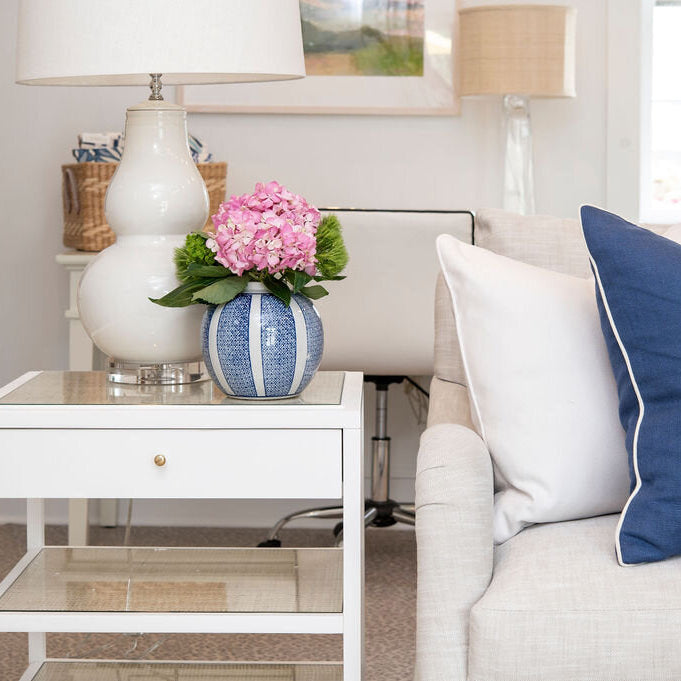 Living room with a white sofa, decorative pillows, and a side table with a lamp and flowers.