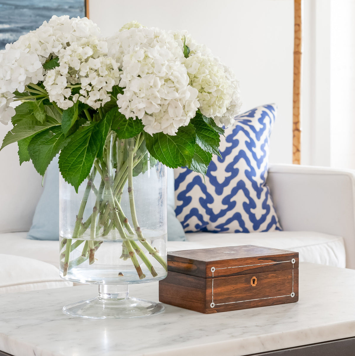 White flowers in a vase on a marble coffee table with a lamp and sofa in the background.