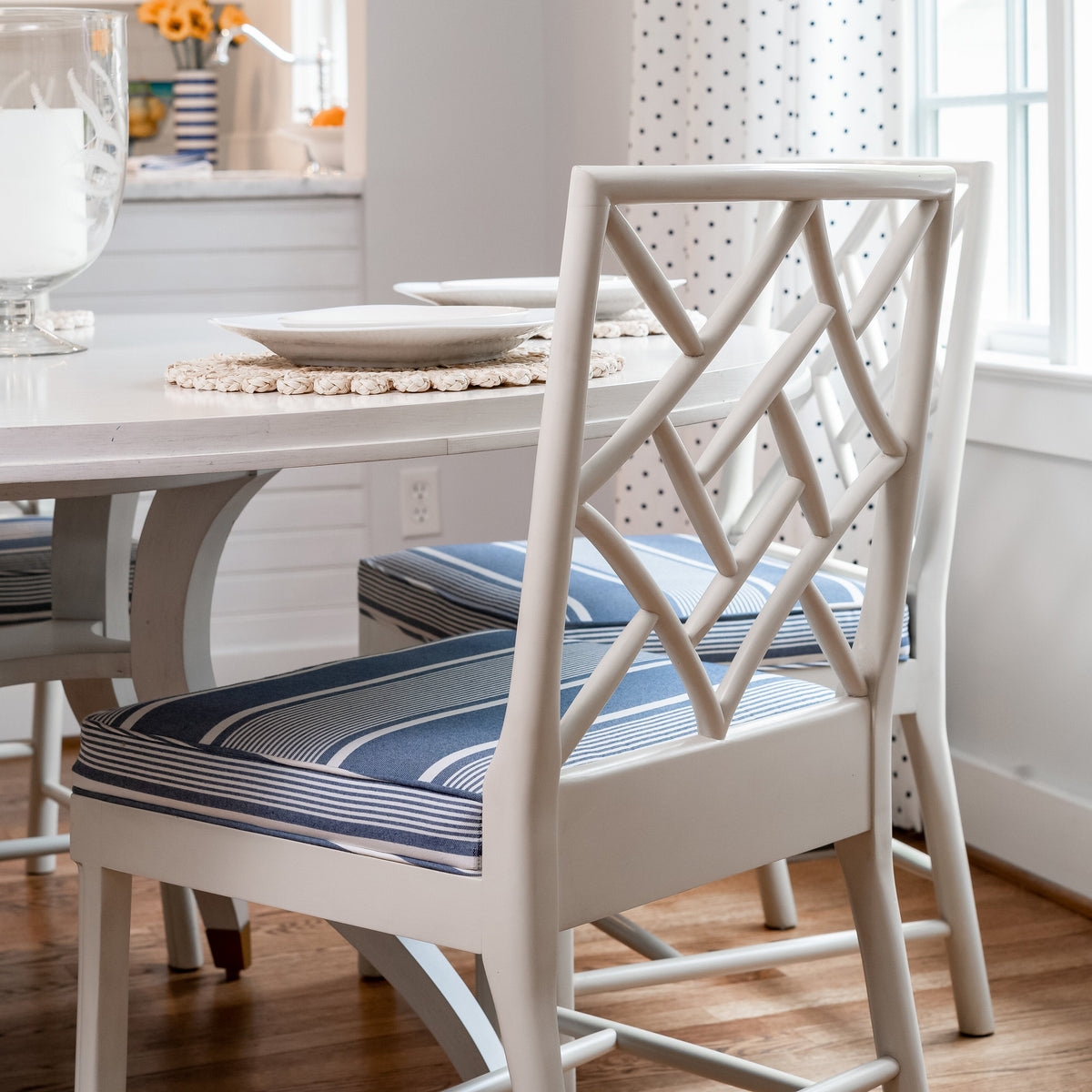 Dining room with white chairs, striped cushions, and a window with polka dot curtains.