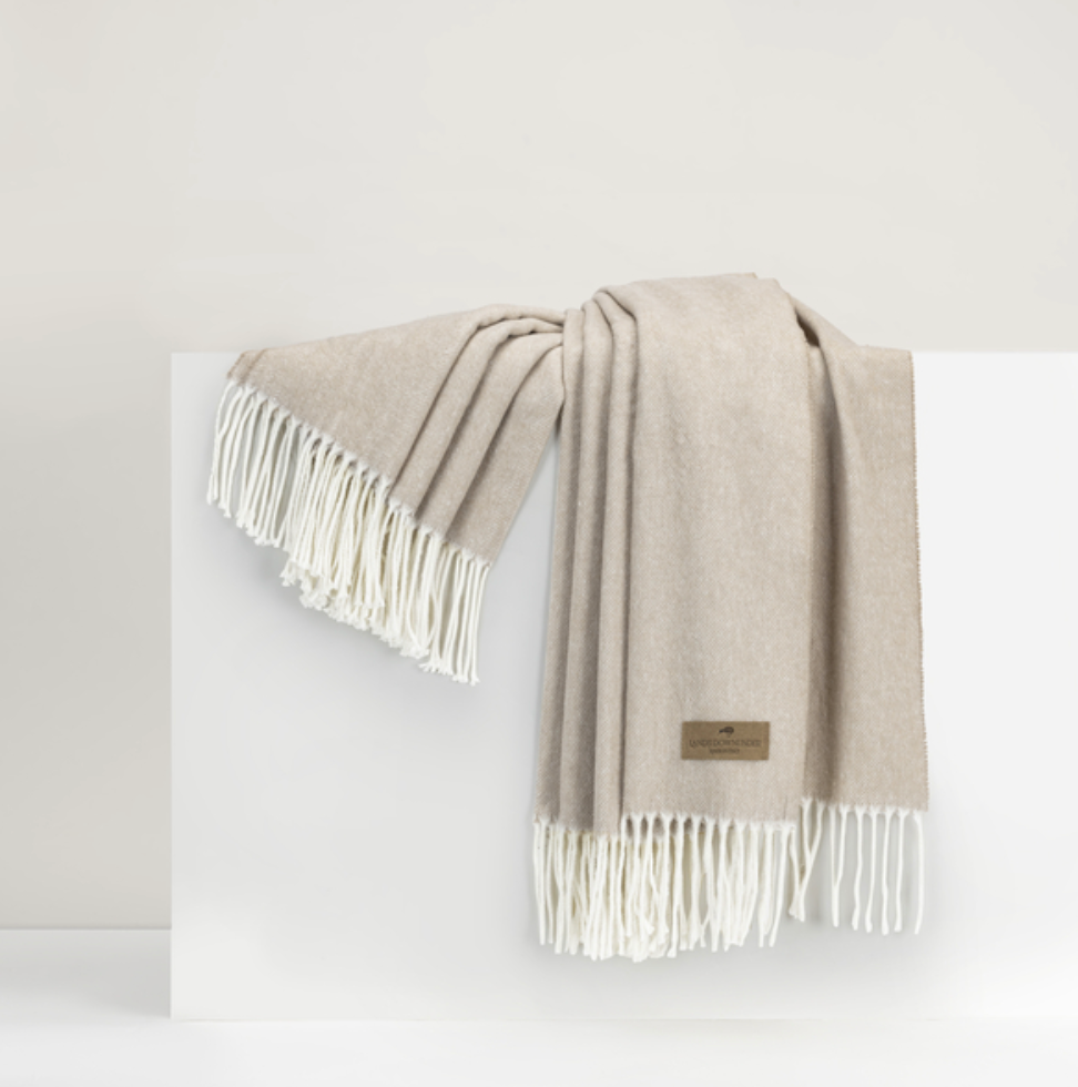 A beige Italian herringbone throw with fringes displayed on a white surface.